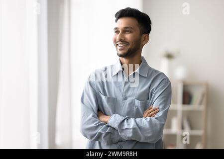 Indian man standing with arms crossed smiling looking away Stock Photo