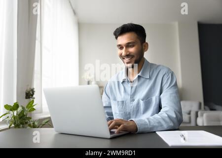 Smiling Indian man enjoy remote online work at home Stock Photo