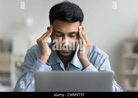 Man sitting at desk with laptop, touch temples, having headache Stock Photo