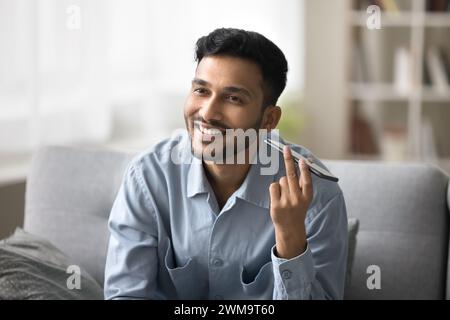 Smiling young Indian man listening pleasant audio message Stock Photo