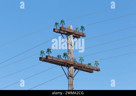 Old wooden electric pole with wires and glass insulators against a blue sky Stock Photo