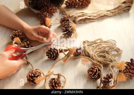 Woman's hands make wall decorations from pine cones and jute rope Stock Photo