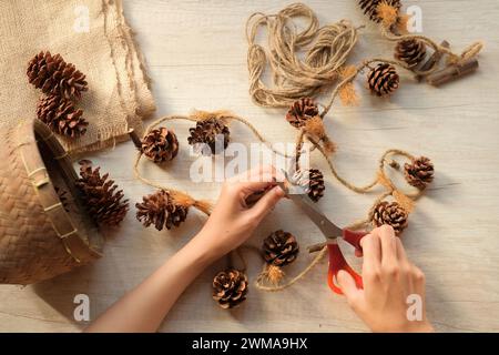 Woman's hands make wall decorations from pine cones and jute rope Stock Photo
