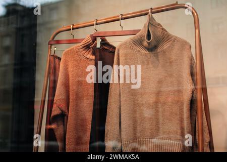 Brown beige knitted sweaters hanging in a row on a hanger in the window of a women's fashion store Stock Photo