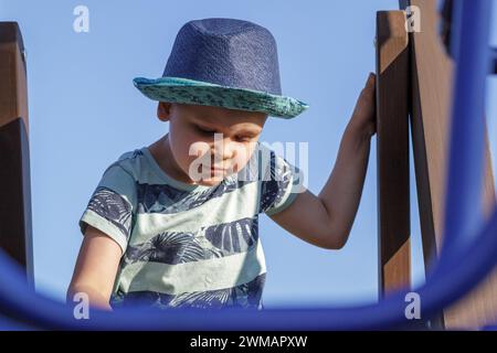 A child climbs up in a park on a playground on a hot summer day. Children's playground in a public park, entertainment and recreation for children. Stock Photo