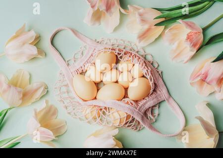 String bag with Easter eggs and yellow tulips on light green background. Top view, flat lay. Stock Photo