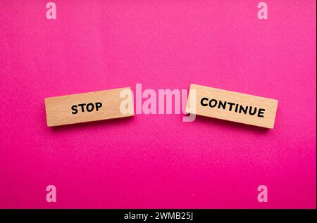Stop or continue words written on wooden blocks with pink background. Conceptual symbol. Copy space. Stock Photo