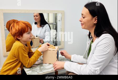 Female psychologist working with boy patient in office while play therapy session. Mental health for kids Stock Photo