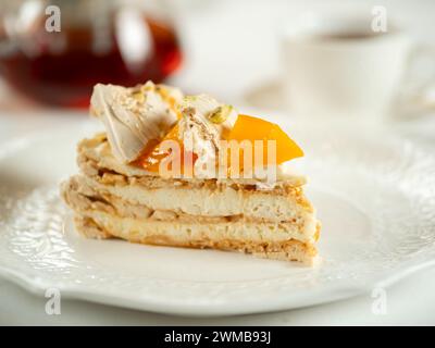 Puff layered cake with cream of cream-cheese, decorated fresh persimmons. Delicious and eye-catching piece of layered cake decorated crispy meringue and orange persimmons Stock Photo