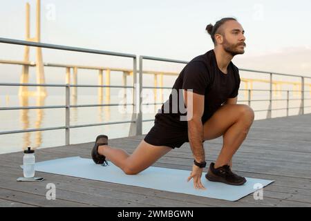 Motivated young man in sporty attire doing leg stretches outside Stock Photo