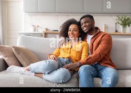 Black young millennial couple find relaxation on couch embracing indoor Stock Photo