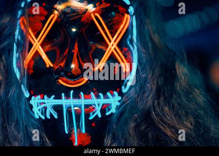 Close up of person with long disheveled hair in a lighting neon glowing mask. Stock Photo