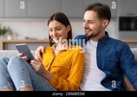 Couple smiling at tablet screen, resting on couch at home Stock Photo