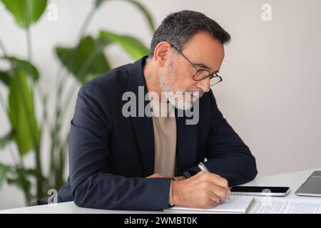 A professional middle-aged man with glasses focused on signing documents at his modern office desk Stock Photo