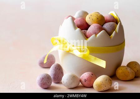 Colored chocolate easter eggs candy in eggshell shaped bowl on pink background, easter sweets, decoration Stock Photo