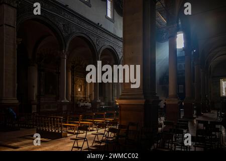 June 4, 2023 - Ferrara. The dark and silent interior of an ancient church. Light filtering through the rose window, illuminating the chairs and benche Stock Photo