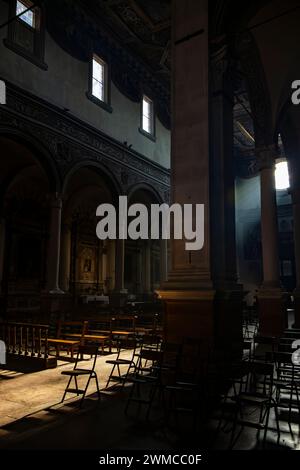 June 4, 2023 - Ferrara. The dark and silent interior of an ancient church, with light filtering through the rose window, illuminating the chairs and b Stock Photo