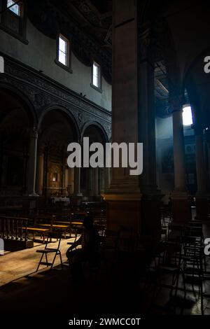 June 4, 2023 - Ferrara. The dark and silent interior of an ancient church. Light filtering through the rose window, illuminating the chairs and benche Stock Photo