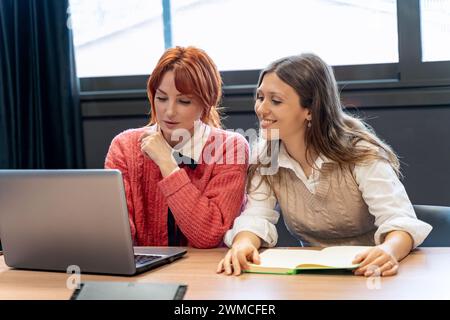 Two female professionals discussing over a laptop in a modern office, focused and engaged.  Stock Photo