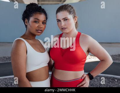 Portrait of two young plus-size females in sportswear. Two women of different ethnicities standing together after workout outdoors. Stock Photo