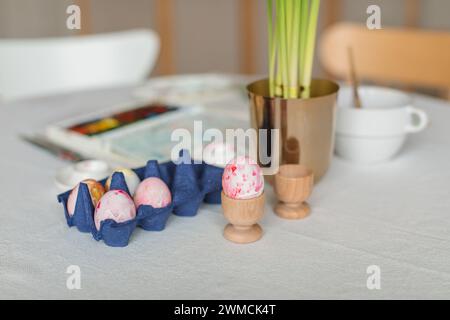 Close-up of a paintbrush, paint palette and carton of eggs being painted for Easter decorations with narcissus flowers on a table Stock Photo