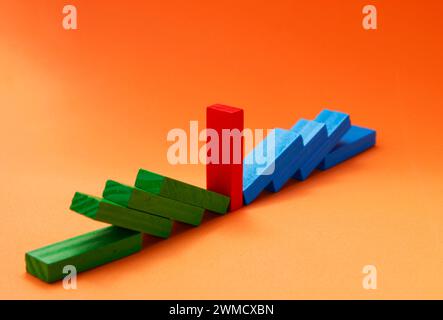 Wooden figures of different colors where in the middle one remains standing and the rest falls Stock Photo