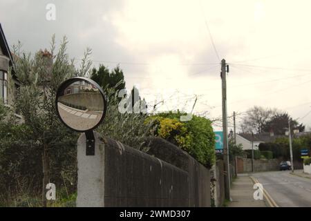 A photo of a convex steel mirror on a wall outside of a house beside a road. Stock Photo