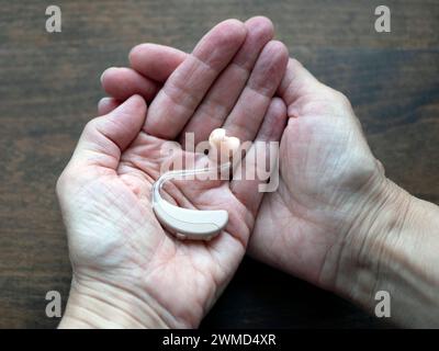 Hearing aid in hands, small electronic device that person wears behind the ear, selective focus. World hearing day Stock Photo