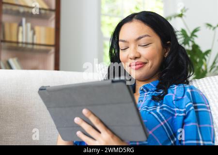 Young biracial woman smiles while using a tablet at home Stock Photo