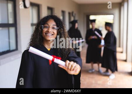 Teenage biracial girl proudly displays her diploma at graduation Stock Photo