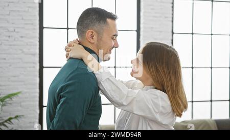 Couple embracing in a bright, modern living room, sharing a moment of affection with smiles. Stock Photo
