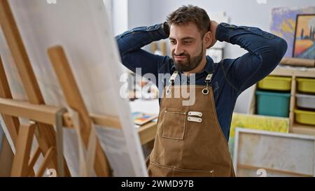 Relaxed young hispanic man, a portrait of handsome bearded artist, focused and concentrating on drawing with paintbrushes at art studio, perfecting ca Stock Photo