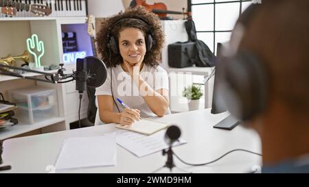 Live on air, inside the buzzing radio studio, smiling reporters in casual attire interview guests, taking vivid notes, and presenting news catchily Stock Photo