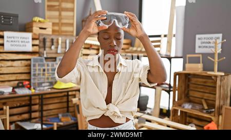 Stunning african american female carpenter, concentrating on her craft indoors, proudly standing at her woodworking studio wearing security glasses am Stock Photo