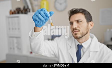Handsome hispanic man with beard, in lab coat, examines test tube in medical laboratory. Stock Photo