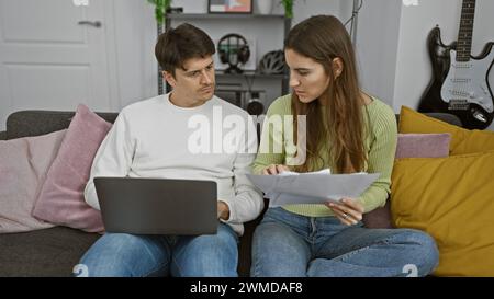 Concerned couple reviewing documents together in a cozy living room with a laptop and guitar in the background Stock Photo