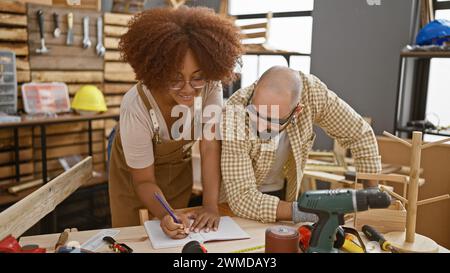Two smiling carpenters confidently taking notes in their woodworking workshop Stock Photo
