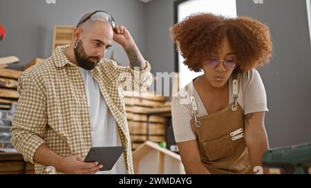 Two professional carpenters speak business over touchpad in bustling carpentry workshop Stock Photo