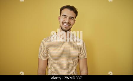 Handsome young hispanic man smiling against a yellow background, exuding casual confidence and charm. Stock Photo