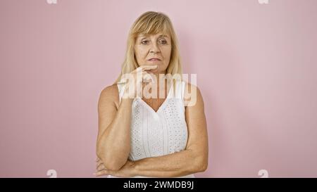 Middle age beautiful blonde woman wears serious expression, standing confidently over isolated pink background, deep in thought Stock Photo