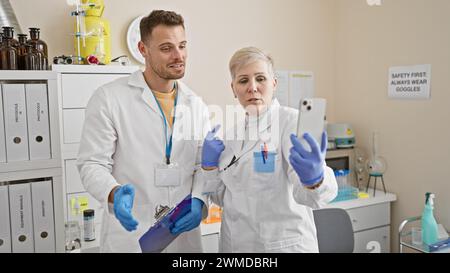 A man and woman, both scientists, are analyzing data on a smartphone together in a laboratory setting. Stock Photo