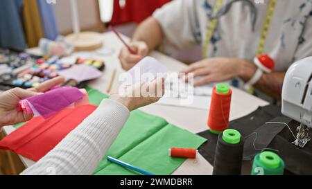 Two tailors working with fabrics and sewing accessories in a tailor shop, crafting custom garments. Stock Photo