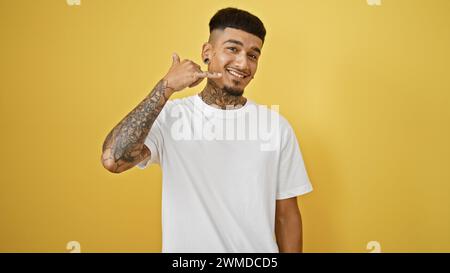 Joyful young latin man showing off phone gesture with his hand, confident and smiling against isolated yellow background Stock Photo