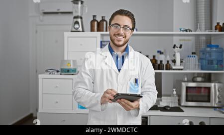 Young hispanic man scientist using touchpad smiling at laboratory Stock Photo