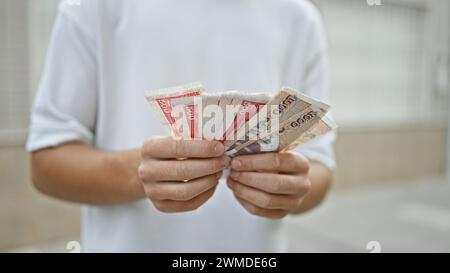 Young handsome hispanic teenager counting stack of iceland krona banknotes on an urban street, exploring finance and investment Stock Photo