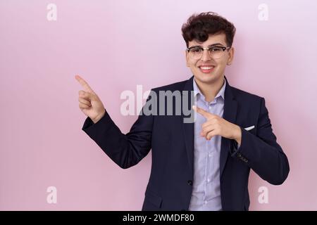 Young non binary man with beard wearing suit and tie smiling and looking at the camera pointing with two hands and fingers to the side. Stock Photo