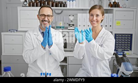 Two smiling scientists clapping hands in applause, celebrating major research breakthrough in their lab Stock Photo