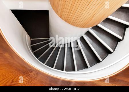 Black spiral staircase goes down in wooden interior, top view, abstract architecture photo background Stock Photo