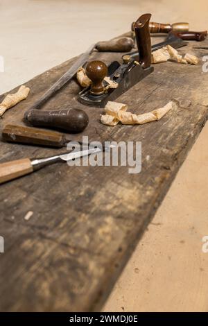 Photo an array of wood carving tools, including chisels and a hand plane, lie on a weathered workbench with wood shavings scattered around, evoking a Stock Photo