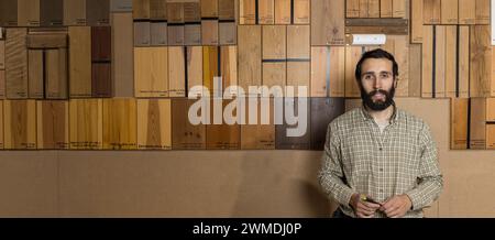 Horizontal photo a bearded woodworker mid adult caucasian stands confidently in his workshop, a wall of labeled wood samples showcasing various specie Stock Photo